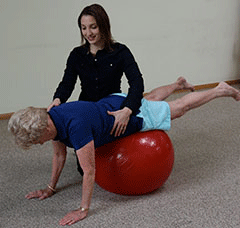 Teresa assisting Alice with plank on physioball